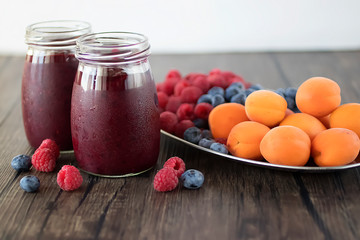 Fruit and berry smoothies and fresh apricots, raspberries and blueberries on an oval metal plate. Gray background.