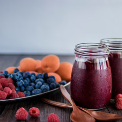 Fruit and berry smoothies and fresh apricots, raspberries and blueberries on an oval metal plate. Gray background.