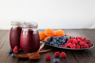 Fruit and berry smoothies and fresh apricots, raspberries and blueberries on an oval metal plate. Gray background.
