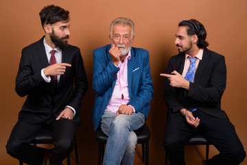 Three multi ethnic bearded businessmen together against brown background