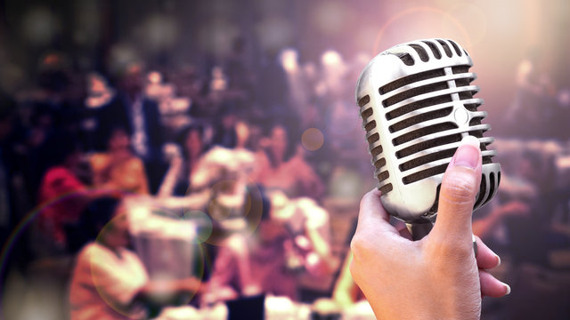 Retro microphone in women hand for speech or singing isolated on black background