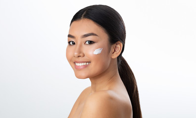 Face care concept. Asian girl applying cream on her cheek