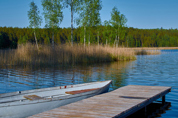 Wooden boat at the pier on the lake, the island and green forest in the background.