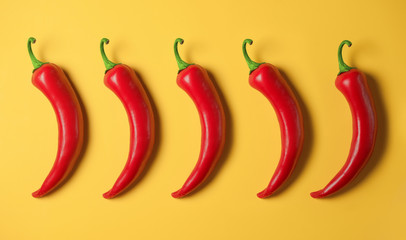 Five hot red peppers on a yellow background.