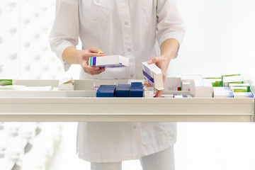 Pharmacist holding medicine box and capsule pack in pharmacy drugstore.