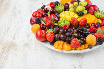 Healthy fruit platter, strawberries raspberries oranges plums apples kiwis grapes blueberries mango persimmon on wooden table, copy space for text, selective focus