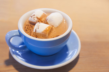 Drink Hot Chocolate topped by Milk Latte Foam with marshmallow in blue ceramic porcelain cup on wooden table background. Relaxed moment with healthy dairy beverage with melted sweets in morning.