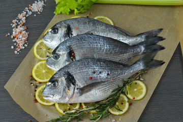 Raw fish with aromatic herbs, spices, salt and lime slices.Raw dorado on dark background .healthy food, cooking, diet, nutrition concept.