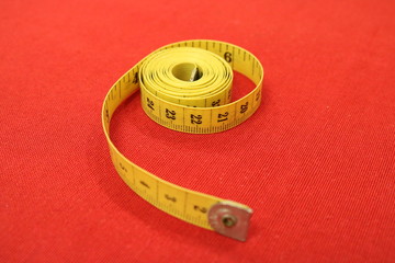 Yellow rolled-up measuring tape of the cutter on the red table. 