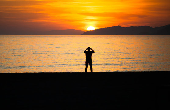 Silhouette of man taking photograph of sunset on beach