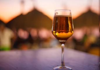 Stemmed glass of beer on beach at sunset