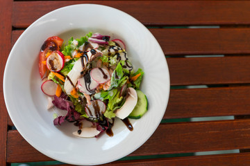 fresh salad with radish, cucumber, tomato and lettuce on white plate