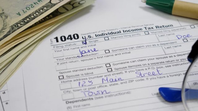 Dollar bills, Pen and Glasses on 1040 Tax Return Form with female name Jane Doe. All data is fictitious and does not disclose personal data. Savings, finances and economy concept 