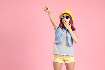 Beautiful young girl in fashion clothing showing finger up on pink background