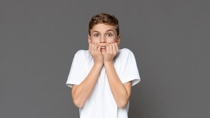 Scared teen boy biting nails in fear