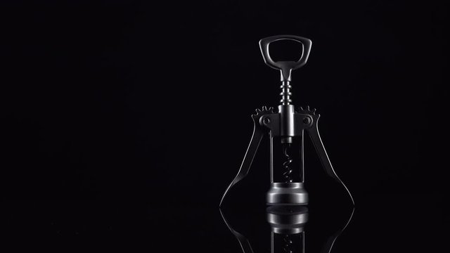 Silver colored bottle opener on black background. Universal shiny corkscrew tool with spiral for opening beverage drinks isolated on dark backdrop with space for text