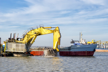 Deepening the water area of the port. A floating excavator loads soil onto a barge.