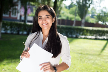 Fototapeta premium portrait of a beautiful indian girl. Business woman smiling holding business papers in her hands. Outdoors