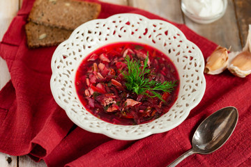 Freshly cooked homemade russian famous soup borsch. Served in white plate with garlic, sour cream, bread, dill. Nourishing tasty meal. Rustic style, close up, wooden background, flat lay, top view