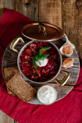 Freshly cooked homemade russian famous soup borsch. Served in cooper pan with garlic, sour cream and dill. Nourishing tasty meal. Rustic style, close up, wooden background, flat lay, top view