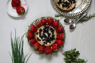 Plate with strawberries and blueberry tart on a white wooden table; top view.