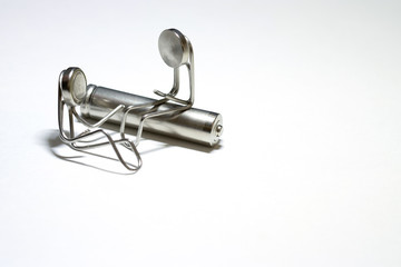 Two little men are made of paper clips. One man is sitting on a cylindrical battery, the other is...
