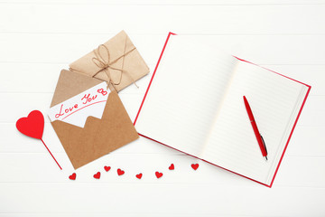 Paper envelopes with red hearts and notepad on white wooden table