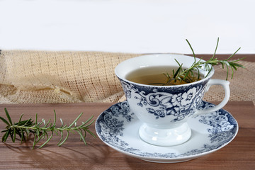 wooden table with cup of tea with branches of rosemary isolated on white background with space for text