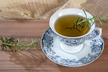 wooden table with cup of tea with branches of rosemary isolated on white background with space for text