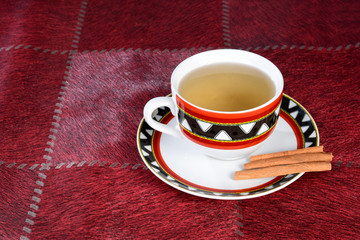 table with cup of tea with pieces of cinnamon isolated on red background with space for text