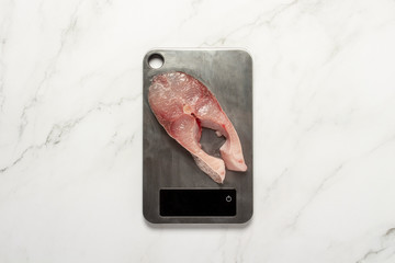 Fish steak on a metal scale on a marble table. Cooking concept. Flat lay, top view