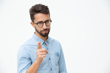 Confident young man pointing at camera. Handsome bearded young man in eyeglasses pointing with finger and looking at camera. Style concept