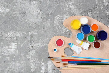 Colorful gouache paints and brushes on grey wooden table