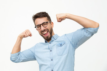 Excited young man showing biceps. Handsome happy young man in eyeglasses showing muscles and smiling at camera on white background. Muscles concept