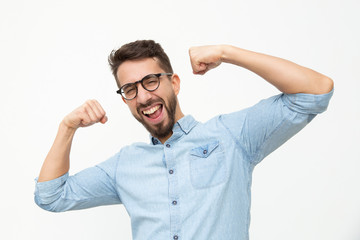 Excited young man showing biceps. Handsome happy young man in eyeglasses showing muscles and...