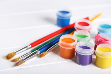 Colorful gouache paints and brushes on white wooden table