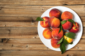 Fototapeta na wymiar Fresh peaches with green leafs in plate on brown wooden table