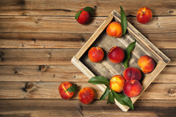 Fresh peaches with green leafs in crate on brown wooden table