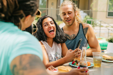 Friends at party laughing at something on cell phone screen. 