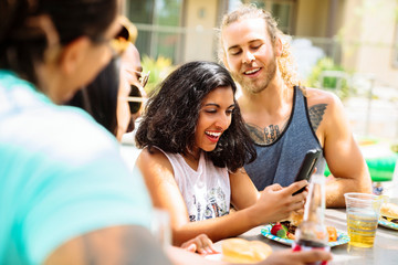 Friends at party laughing at something on cell phone screen. 