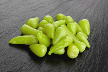 Marinated chili pepper on a slate board. Close-up of several pickled chili peppers on a stone surface.