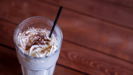 Milkshake in high glass on wooden table. Cold beverage with topping of whipped cream and chocolate...