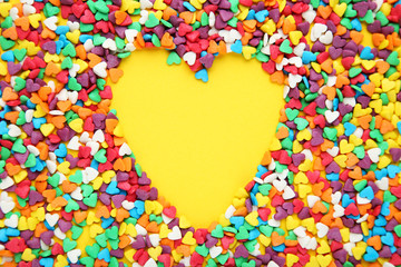 Colorful heart shaped sprinkles on yellow background