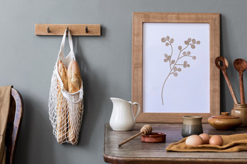  Stylish interior design of kitchen space with mock up photo frame, wooden table, cup of tea, eggs, bagles and kitchen accessories. Cozy home decor of kitchen space. Template. 