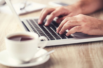 Man working on laptop computer with cup of tea in the office