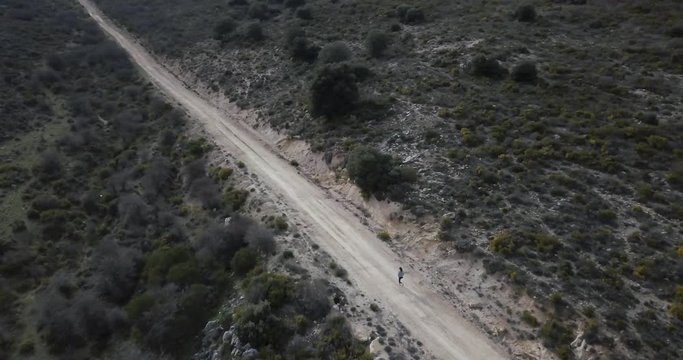 Plano de drone mujer corriendo sola por carretera de tierra a toda velocidad 4K