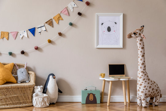 Stylish and beige scandinavian decor of kid room with mock up poster frame, design furnitures, natural toys, hanging colorful flags and balls, teddy bears, plush animal and child accessories. Template