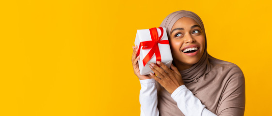 Curious afro muslim girl shaking gift box present, listening what's inside