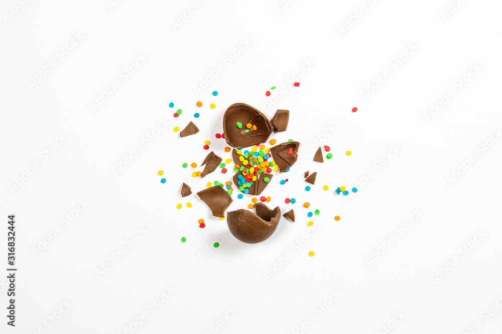 Wall mural Broken Easter chocolate eggs and colorful decorations on a light background. Easter concept, easter treats. Flat lay, top view