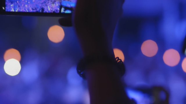 Woman taking video shoot of music show holding smartphone in hand in nightclub. Female fan recording performance using phone in interior with blue light. Blurred view of crowd is on party. Concept